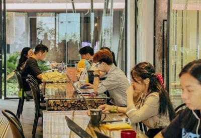 Bright communal coworking area with people working at a long rustic wooden table.