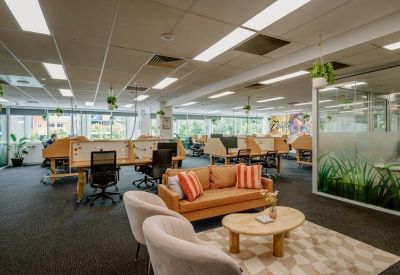 Spacious open-plan office with timber desks, a tan leather sofa, and potted plants.
