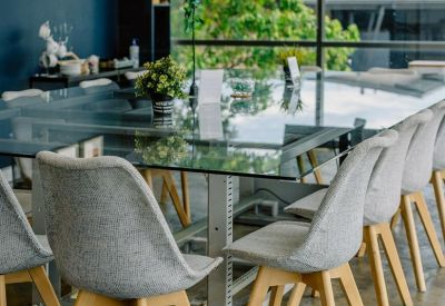Professional boardroom featuring a large glass table, grey upholstered chairs, and a neon sign.