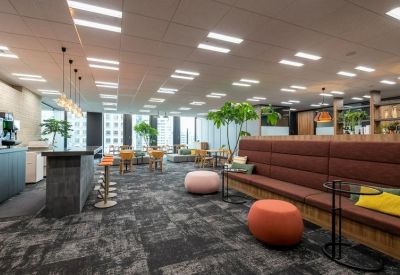 Spacious communal lounge featuring a long brown sofa, cafe counter, and potted trees.