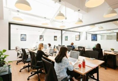Open-plan office space with employees working at long wooden desks under bright skylights.