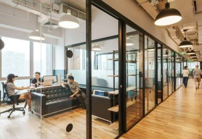 Long glass-walled corridor lined with private office suites and hanging industrial lamps.