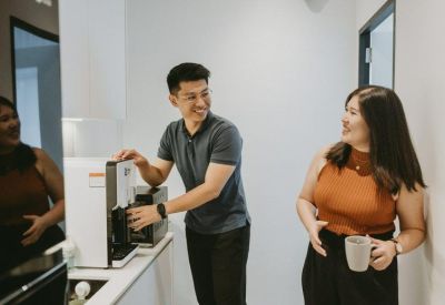 Communal kitchen area featuring people interacting near a modern coffee machine and water dispenser.