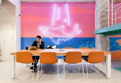 Modern lounge area featuring a vibrant pink wall with a neon shark light and orange seating.