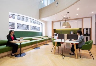 Open-plan coworking area featuring green bench seating and professionals working at individual tables.