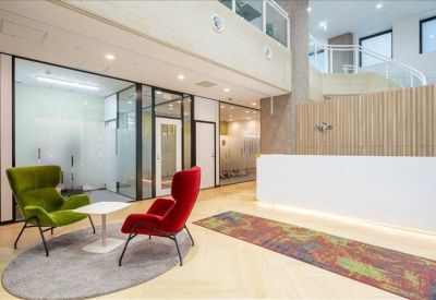 Minimalist reception lounge featuring vibrant green and red wingback chairs on a grey circular rug.