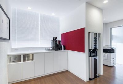 Bright office kitchen with white cabinets, a coffee machine, and a bold red accent wall.