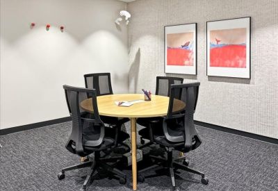 A private four-person meeting room with a round wooden table and grey patterned carpet.