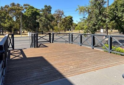 An outdoor wooden decking area with black cross-patterned fencing overlooking a parkland setting.