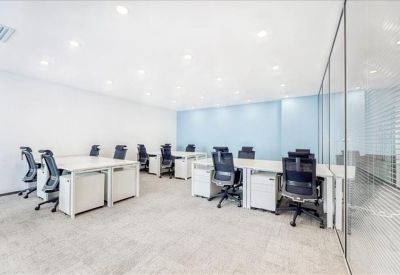 Bright open-plan office space with several rows of white desks and ergonomic chairs.