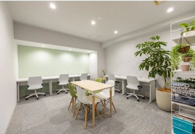 Meeting room with a central wooden table, colorful chairs, and a green accent wall nook with desks.