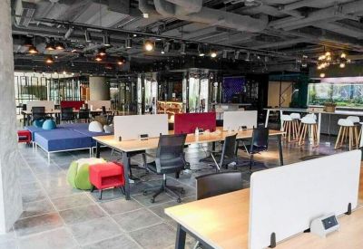Open-plan office area with long desks, ergonomic chairs, and industrial ceiling details.