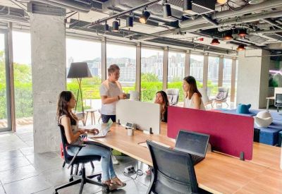Collaborative meeting space with a long wooden table and people working near large windows.