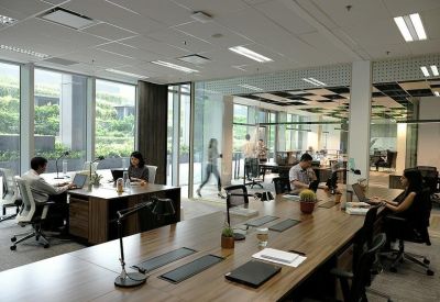 Open-plan office with wooden desks and glass partitions overlooking greenery.