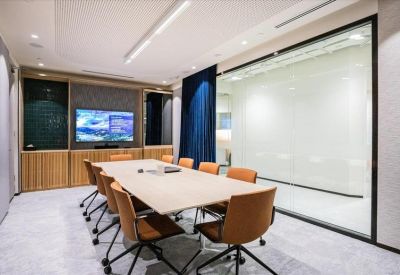 Executive meeting room with a wooden table, orange chairs, and a large wall-mounted display screen.