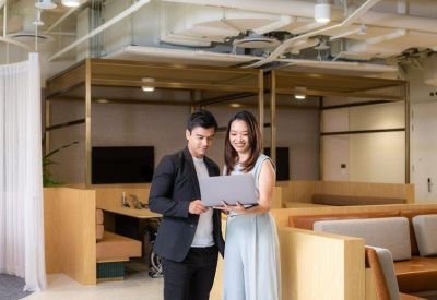 Two colleagues using a laptop in a modern coworking space with wood-paneled booths.