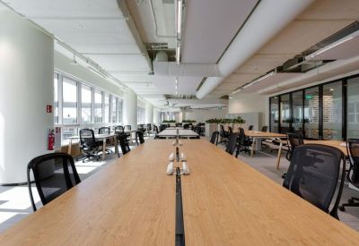 Long wooden hot-desking station in a bright open-plan office with large windows.