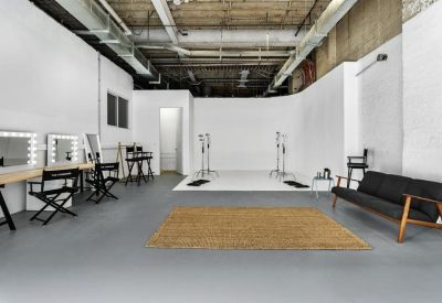 Professional photography or film studio with white walls, lighting gear, and a black sofa.
