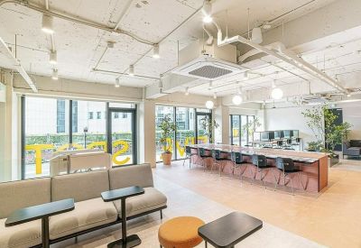 Bright open-plan coworking space with long wooden tables, soft seating, and large windows.