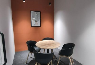 Small breakout room with a round wooden table and four black chairs against an orange wall.