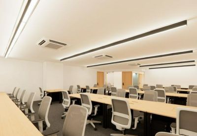 Bright open-plan office with rows of white chairs and long wooden desks.