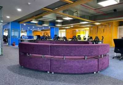 Contemporary open-plan workspace featuring a curved purple modular sofa and bright blue accents.