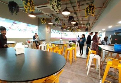 Spacious communal cafe with yellow stools, black round tables, and hanging plants.