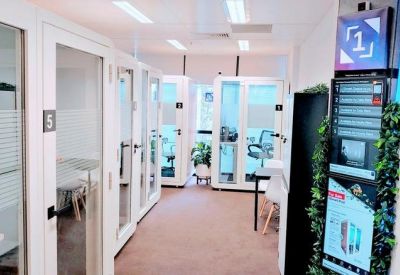 A hallway lined with modern acoustic work pods and a digital directory with greenery.