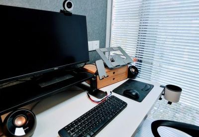 Single person workstation with a large monitor, keyboard, and views through venetian blinds.