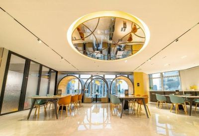 Spacious coworking area with wooden tables, colorful chairs, and a unique circular ceiling mirror.
