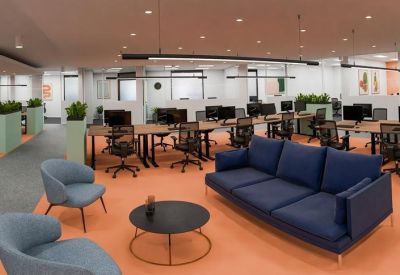 Modern lounge area with a navy blue sofa, grey armchairs, and workstations in the background.
