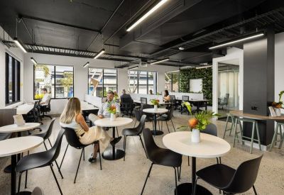 Spacious communal coworking space with round tables, black chairs, and a lush green plant wall.