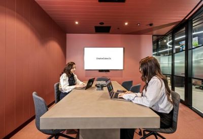 Cozy meeting room with pink walls, a large screen, and a concrete table.