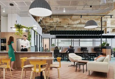 Spacious communal breakout area with a kitchen, dining tables, lounge seating, and hanging greenery.