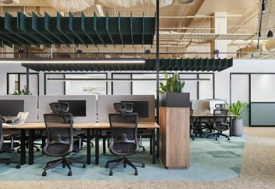 Modern open-plan workspace with ergonomic chairs, light wood desks, and acoustic ceiling baffles.