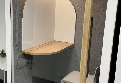 Modern private phone booth with wood-toned desk and acoustic grey walls.