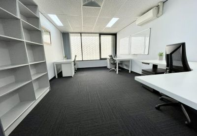 Spacious open-plan office with white desks, black chairs, and a large bookshelf.
