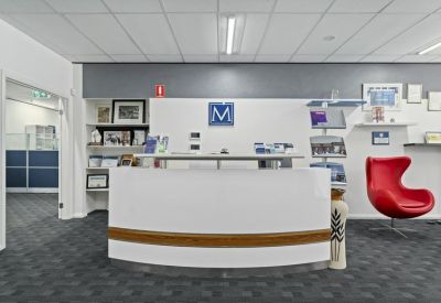 Bright reception area featuring a curved white desk and a red designer chair.