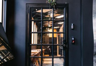 Industrial-style black framed glass door leading into a vibrant workspace.