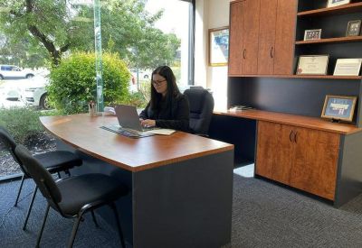 Professional workspace with a wood-finish desk, laptop, and matching cabinetry near a bright window.