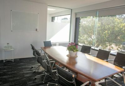 Bright boardroom with a large wooden table, black chairs, and a whiteboard.