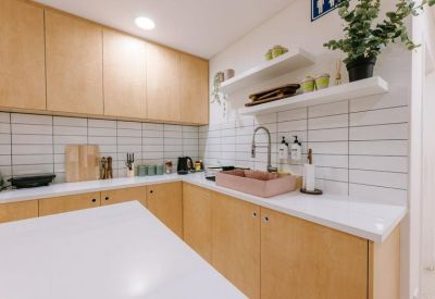 Modern communal kitchen with wooden cabinetry, white subway tiles, and a pink stone sink.