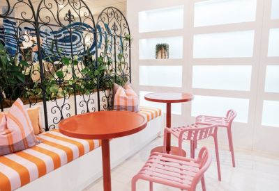 Relaxed breakout area with orange tables, pink chairs, and a decorative wrought iron screen.