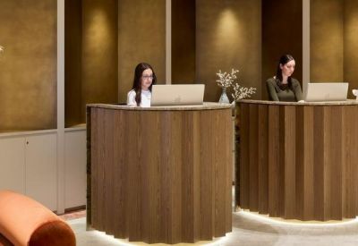Warm timber-clad reception desks with two staff members and decorative vases.