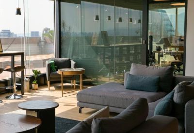 Sunny lounge area with plush grey seating and city views through large windows.