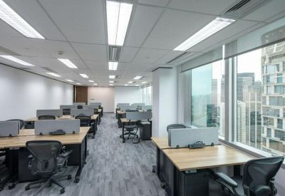 Bright open-plan office with rows of wooden desks and large windows overlooking the city.
