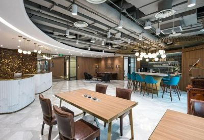 Bright breakout space with wooden dining tables and blue chairs under industrial ceilings.