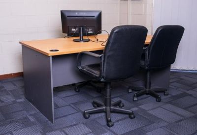 Close-up of a workstation with a computer monitor and dual black office chairs.