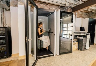 Single-person private acoustic phone booth with a glass door in a coworking space.