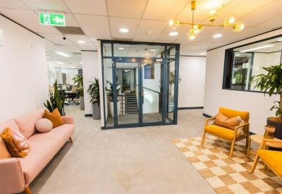 Bright reception lounge with a pink velvet sofa, yellow armchairs, and glass entry doors.